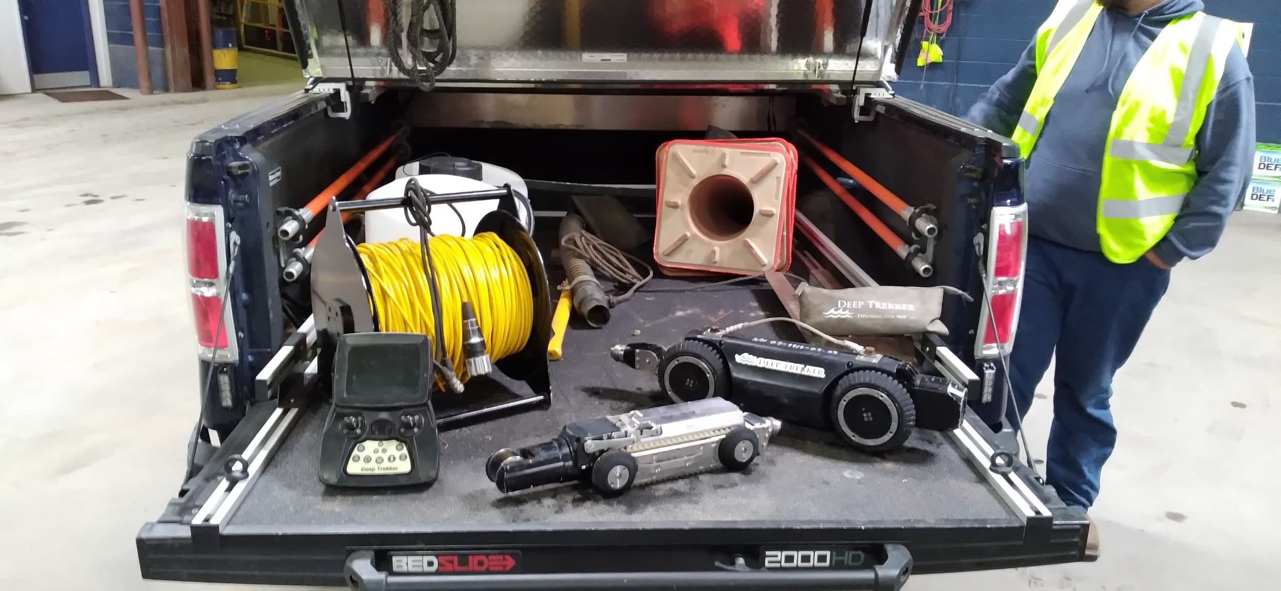 Man standing beside back of pickup truck with Deep Trekker DT340 and DT320 mini pipe crawlers in the back of the truck.