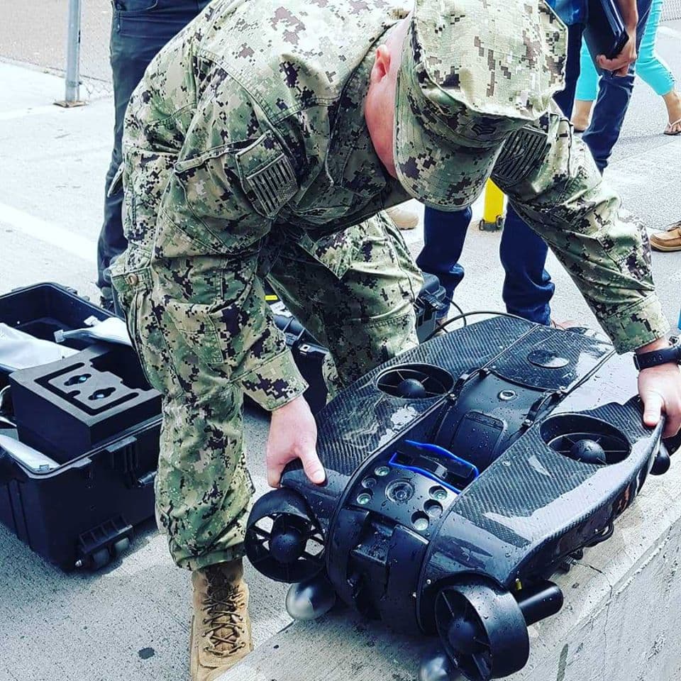 Defense employee lowering Deep Trekker REVOLUTION ROV into water from concrete barrier